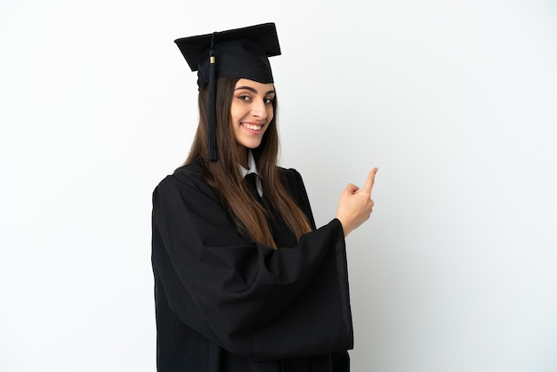 Young university graduate isolated on white background pointing back