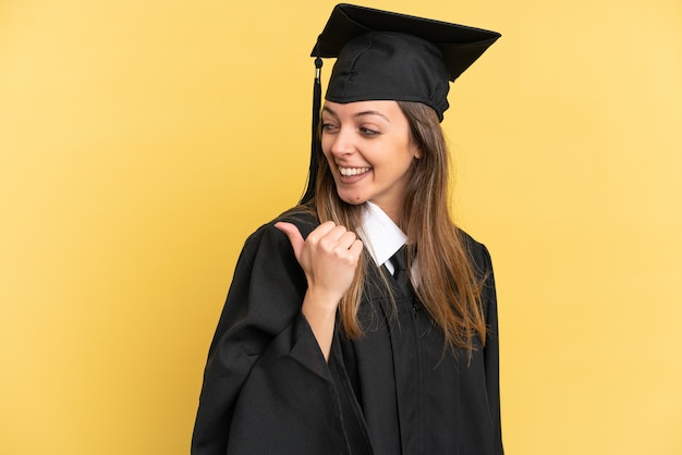 Young university graduate isolated on yellow background pointing to the side to present a product