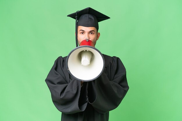 Young university graduate man over isolated background shouting through a megaphone