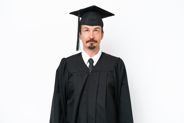 Young university graduate man isolated on white background and looking up