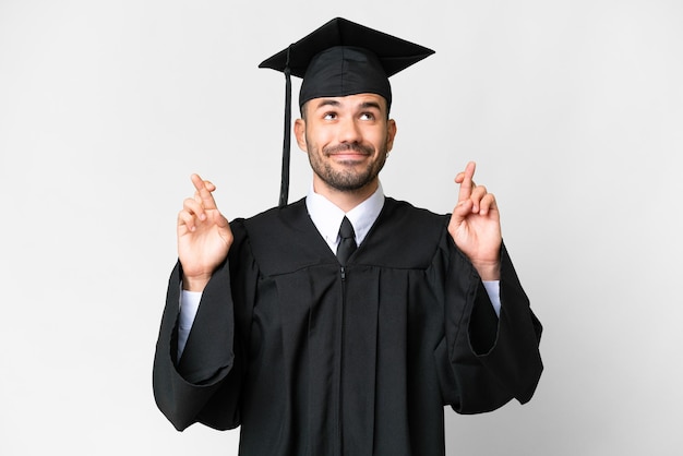 Young university graduate man over isolated white background with fingers crossing