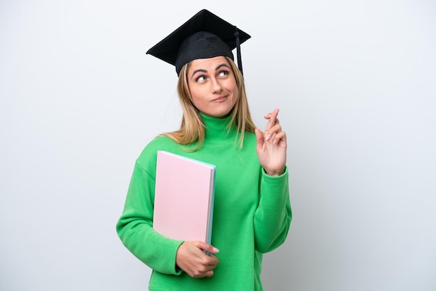 Young university graduate woman isolated on white background with fingers crossing and wishing the best