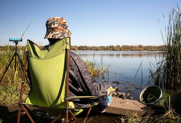 Young unrecognizable guy fisherman catches fish sitting in a chair on the bank of a river or lake