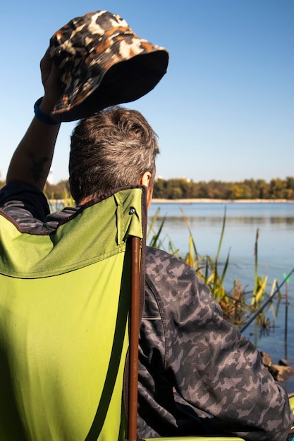 Young unrecognizable guy fisherman catches fish sitting in a chair on the bank of a river or lake