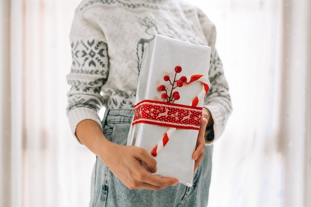 Young unrecognizable woman holds in a gift box in metallic paper with red twine and candy