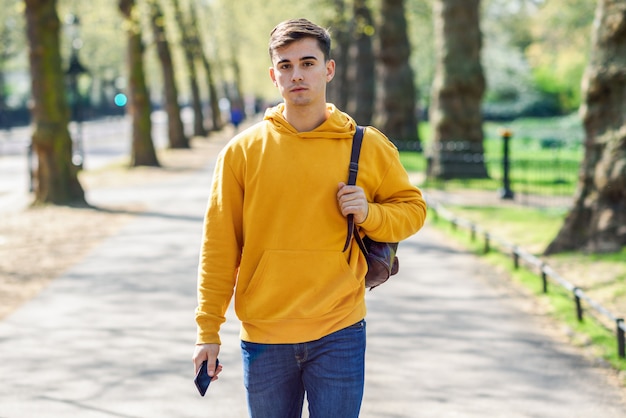 Young urban man using smartphone walking in street in an urban park in London.