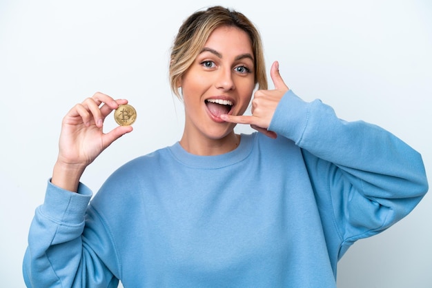 Young Uruguayan woman holding a Bitcoin isolated on white background making phone gesture Call me back sign