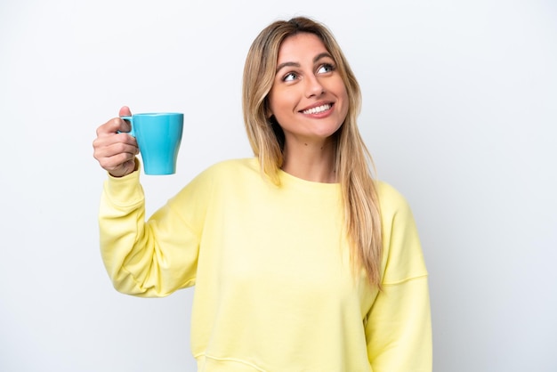 Young Uruguayan woman holding cup of coffee isolated on white background looking up while smiling