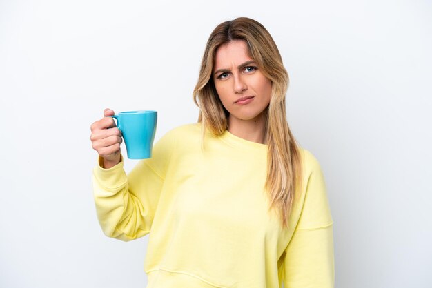 Photo young uruguayan woman holding cup of coffee isolated on white background with sad expression