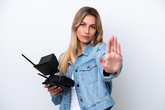 Young Uruguayan woman holding a drone remote control isolated on white background making stop gesture