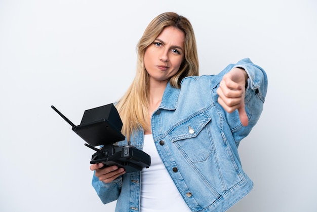 Young Uruguayan woman holding a drone remote control isolated on white background showing thumb down with negative expression