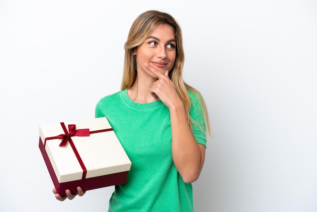 Young Uruguayan woman holding a gift isolated on white background thinking an idea and looking side