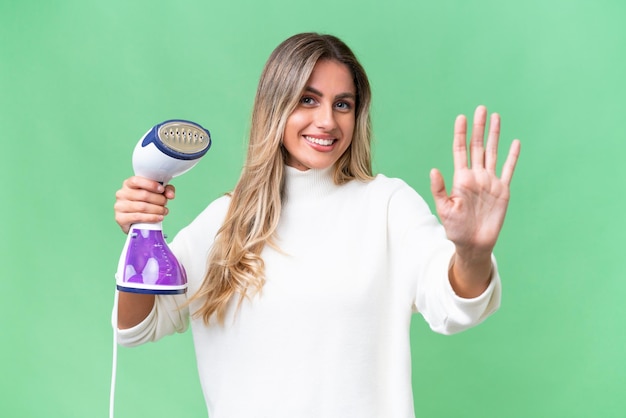 Young Uruguayan woman holding an iron over isolated background saluting with hand with happy expression