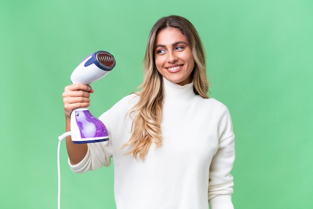 Young Uruguayan woman holding an iron over isolated background with happy expression