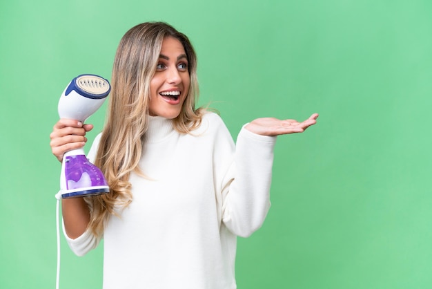 Young Uruguayan woman holding an iron over isolated background with surprise facial expression