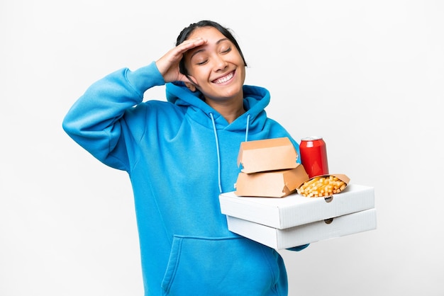 Young Uruguayan woman holding pizzas and burgers over isolated white background smiling a lot