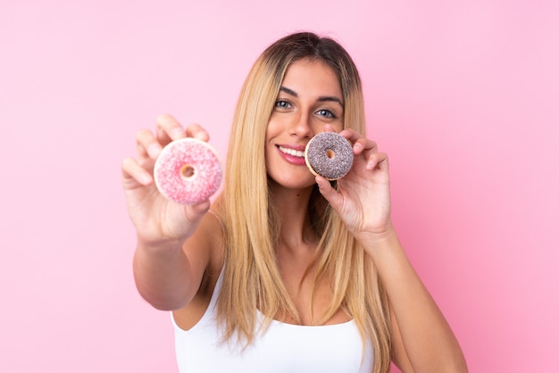 Young Uruguayan woman over isolated wall pink wall holding donuts with happy expression