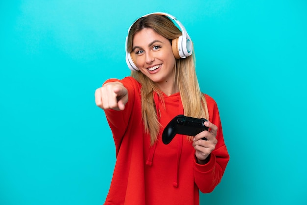 Young Uruguayan woman playing with a video game controller isolated on blue pointing front with happy expression