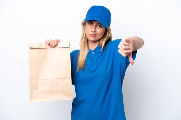 Young Uruguayan woman taking a bag of takeaway food isolated on white background showing thumb down with negative expression