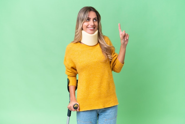 Young Uruguayan woman wearing neck brace and crutches over isolated background intending to realizes the solution while lifting a finger up