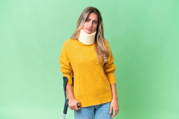 Young Uruguayan woman wearing neck brace and crutches over isolated background with sad expression