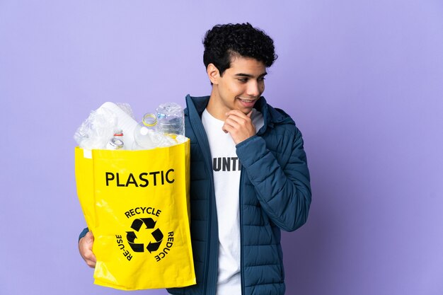 Young Venezuelan man holding a bag full of plastic bottles looking to the side and smiling