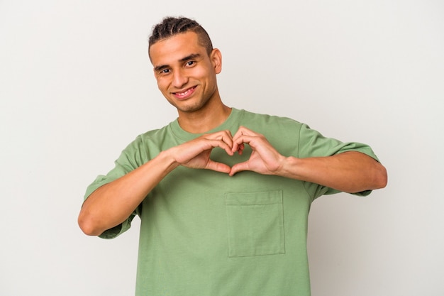 Young venezuelan man isolated on white background smiling and showing a heart shape with hands.