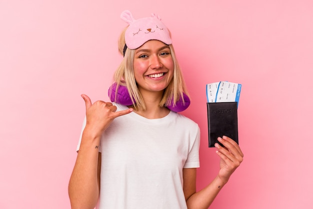 Young venezuelan traveler woman holding a passport isolated on pink wall showing a mobile phone call gesture with fingers.