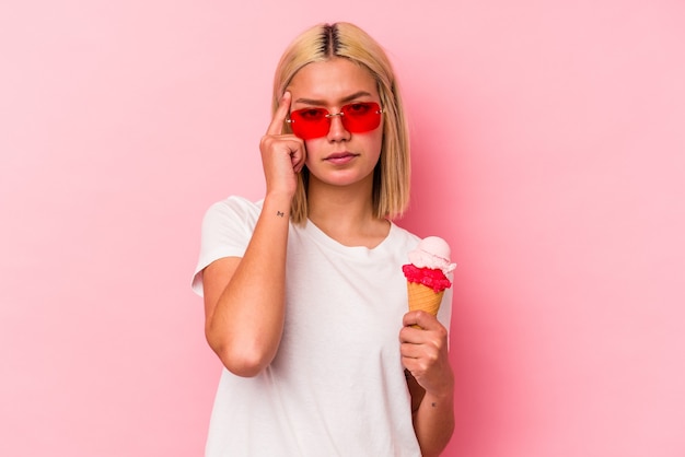 Young venezuelan woman eating an ice cream isolated on pink wall pointing temple with finger, thinking, focused on a task.