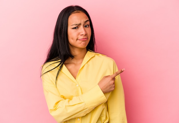 Young Venezuelan woman isolated on pink background smiling and pointing aside, showing something at blank space.