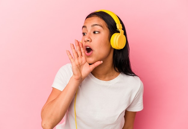 Young Venezuelan woman listening to music isolated on pink wall shouting and holding palm near opened mouth.