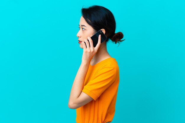 Young Vietnamese woman isolated on blue background keeping a conversation with the mobile phone with someone