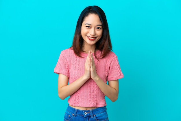 Young Vietnamese woman isolated on blue background keeps palm together. Person asks for something