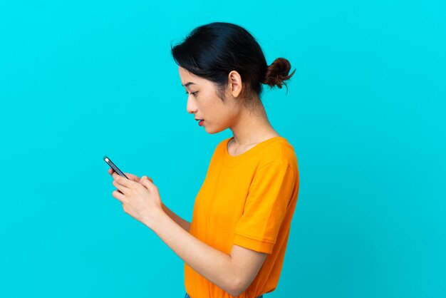 Young Vietnamese woman isolated on blue background sending a message or email with the mobile