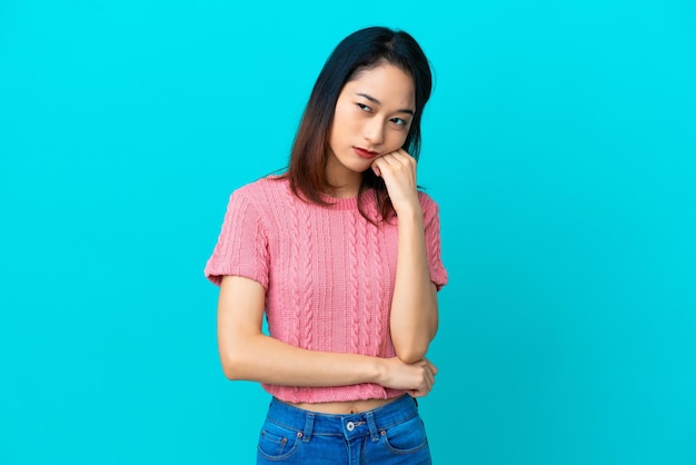 Young Vietnamese woman isolated on blue background with tired and bored expression