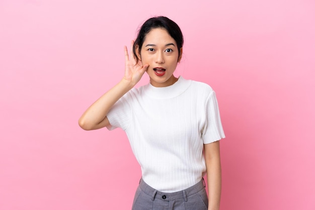 Young Vietnamese woman isolated on pink background listening to something by putting hand on the ear