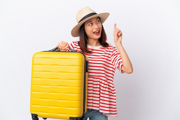 Young Vietnamese woman isolated on white background in vacation with travel suitcase and pointing up