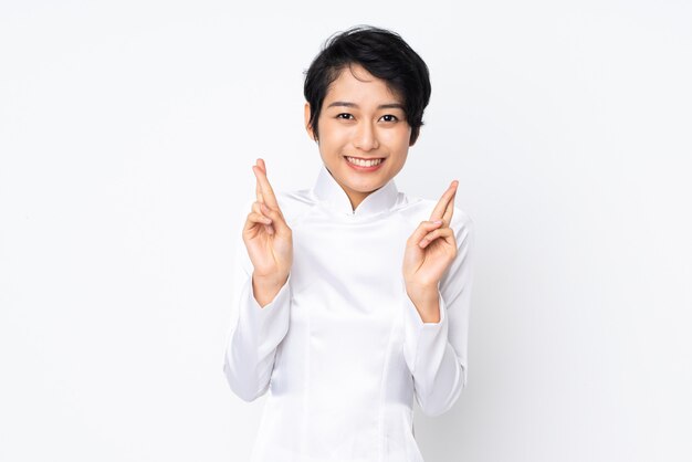 Young Vietnamese woman with short hair wearing a traditional dress over white wall with fingers crossing and wishing the best