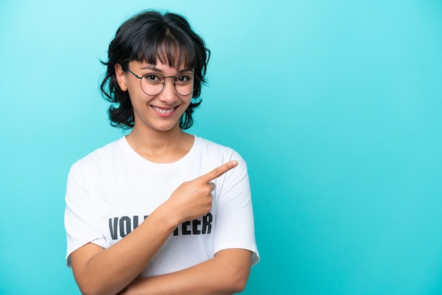 Young volunteer Argentinian woman isolated on blue background pointing to the side to present a product