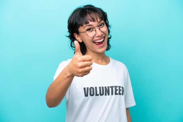 Young volunteer Argentinian woman isolated on blue background with thumbs up because something good has happened