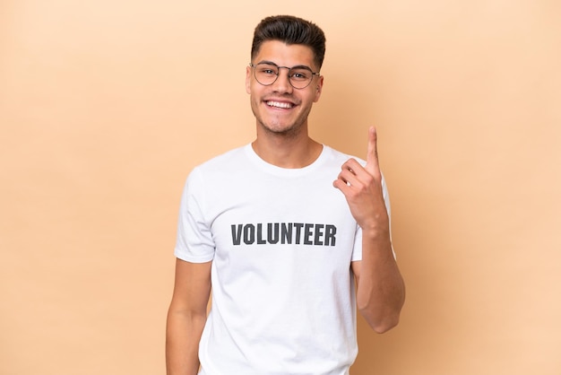 Young volunteer caucasian man isolated on beige background pointing with the index finger a great idea