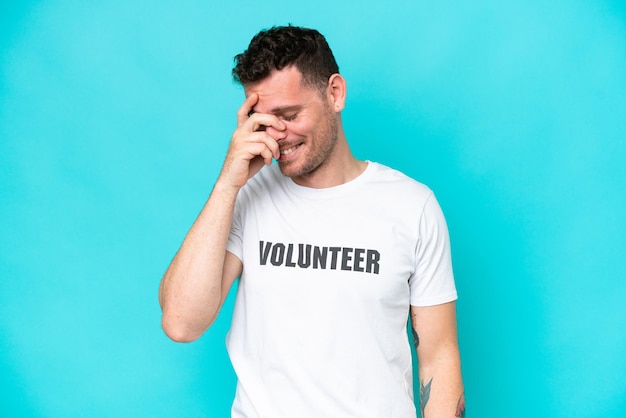 Young volunteer caucasian man isolated on blue background laughing