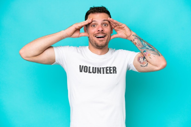 Young volunteer caucasian man isolated on blue background with surprise expression