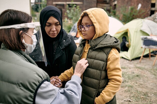 Photo young volunteer in protective mask and screen examining little girl