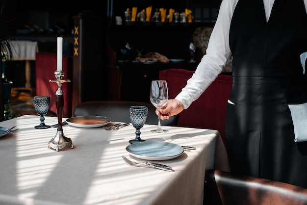 A young waiter in a stylish uniform is engaged in serving the table in a beautiful gourmet restaurant closeup Table service in the restaurant