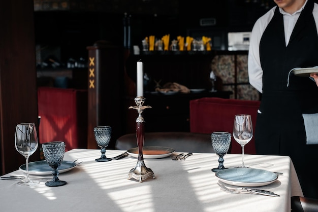 A young waiter in a stylish uniform is engaged in serving the table in a beautiful gourmet restaurant closeup Table service in the restaurant