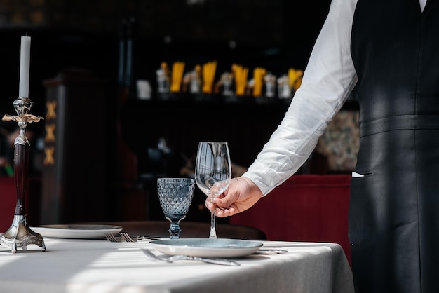 A young waiter in a stylish uniform is engaged in serving the table in a beautiful gourmet restaurant closeup Table service in the restaurant