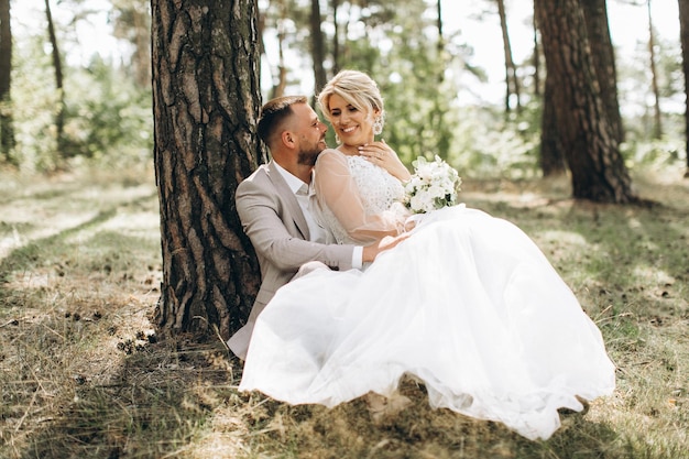 Young wedding couple enjoying romantic moments outside on a summer meadow Copy space Pine forest Green forest are kissing photo portrait Bride and groom