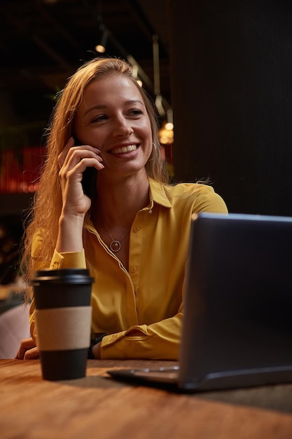 Young well dressed cauasian woman sitting at coffee shop calling by smartphone