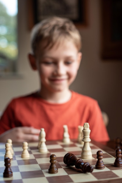 Young white child playing a game of chess on large chess board Chess board on table in front of school boy thinking of next move